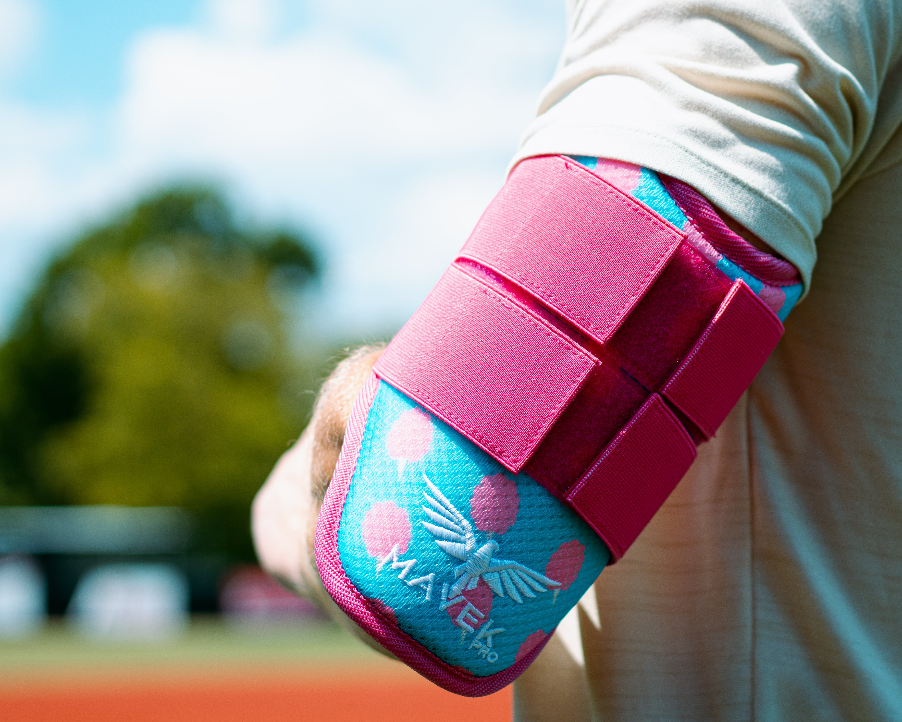 Pink and blue elbow pad with 'MavekPro' branding on a blurred sports field background