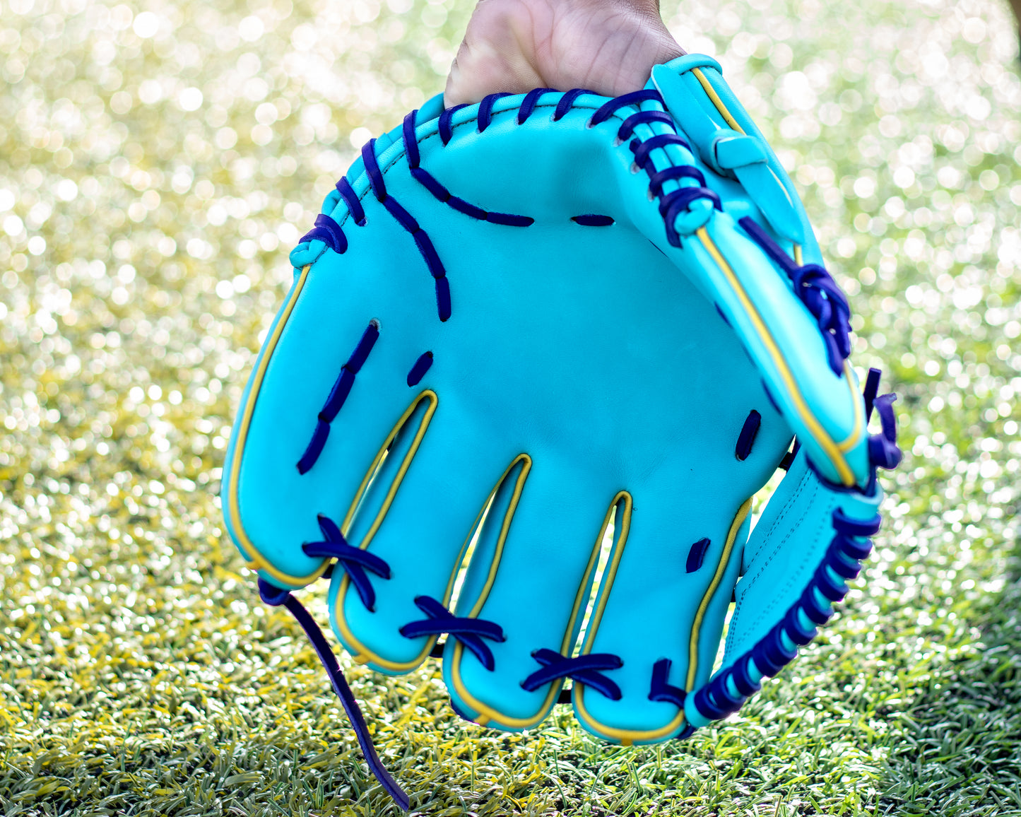 aqua baseball glove with purple stitching held on grass