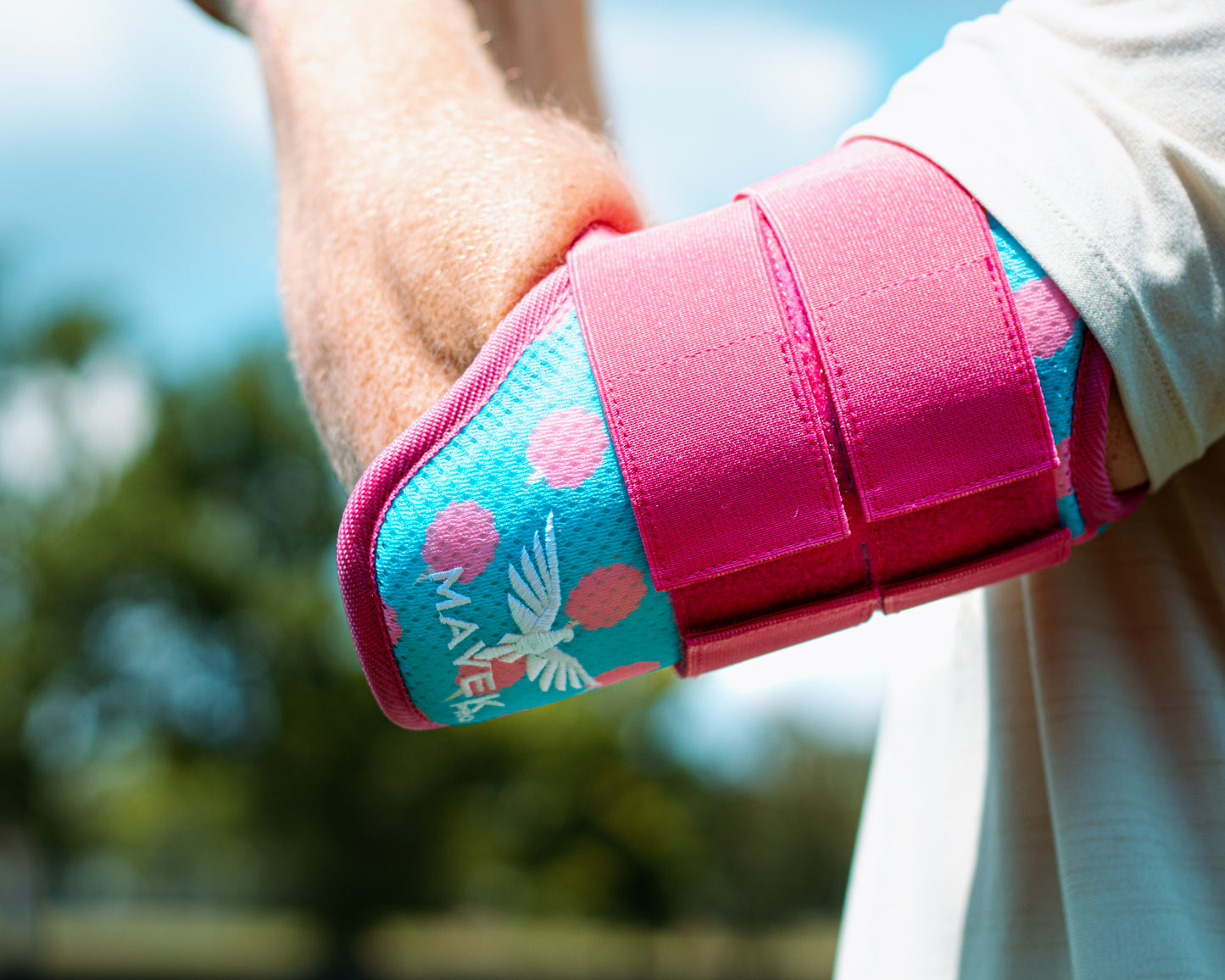 Pink and blue elbow guard with a brand logo on a blurred outdoor background